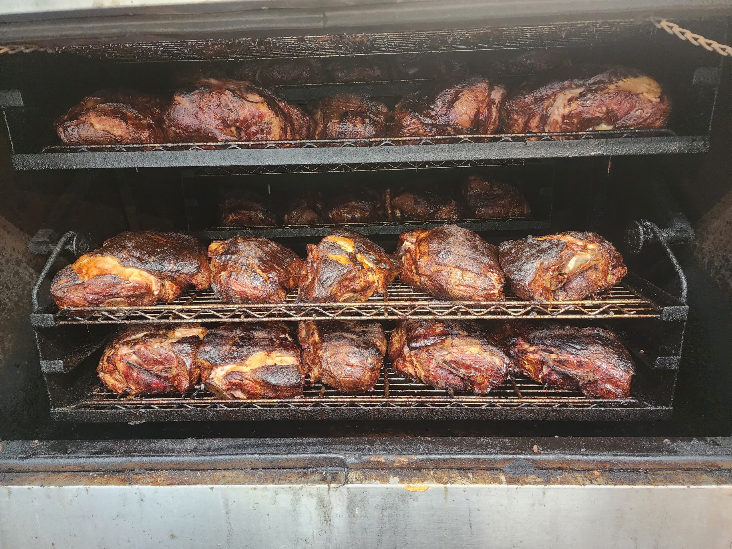 Smoked meats in a commercial smoker, featuring multiple racks filled with juicy, caramelized cuts. Ideal for BBQ enthusiasts or catering events.