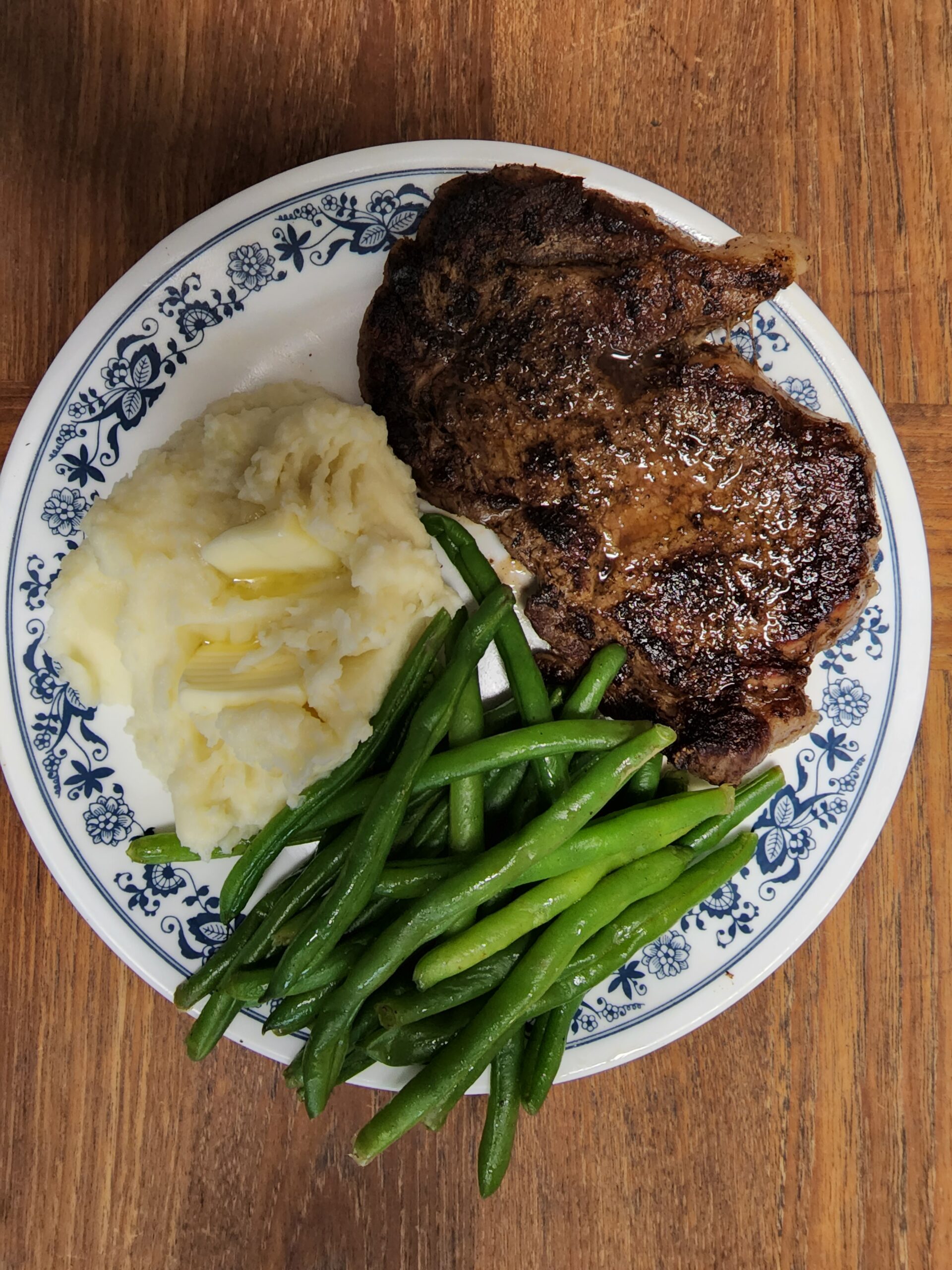 Seared steak with a glossy finish, served alongside creamy mashed potatoes topped with butter and a side of vibrant green beans.